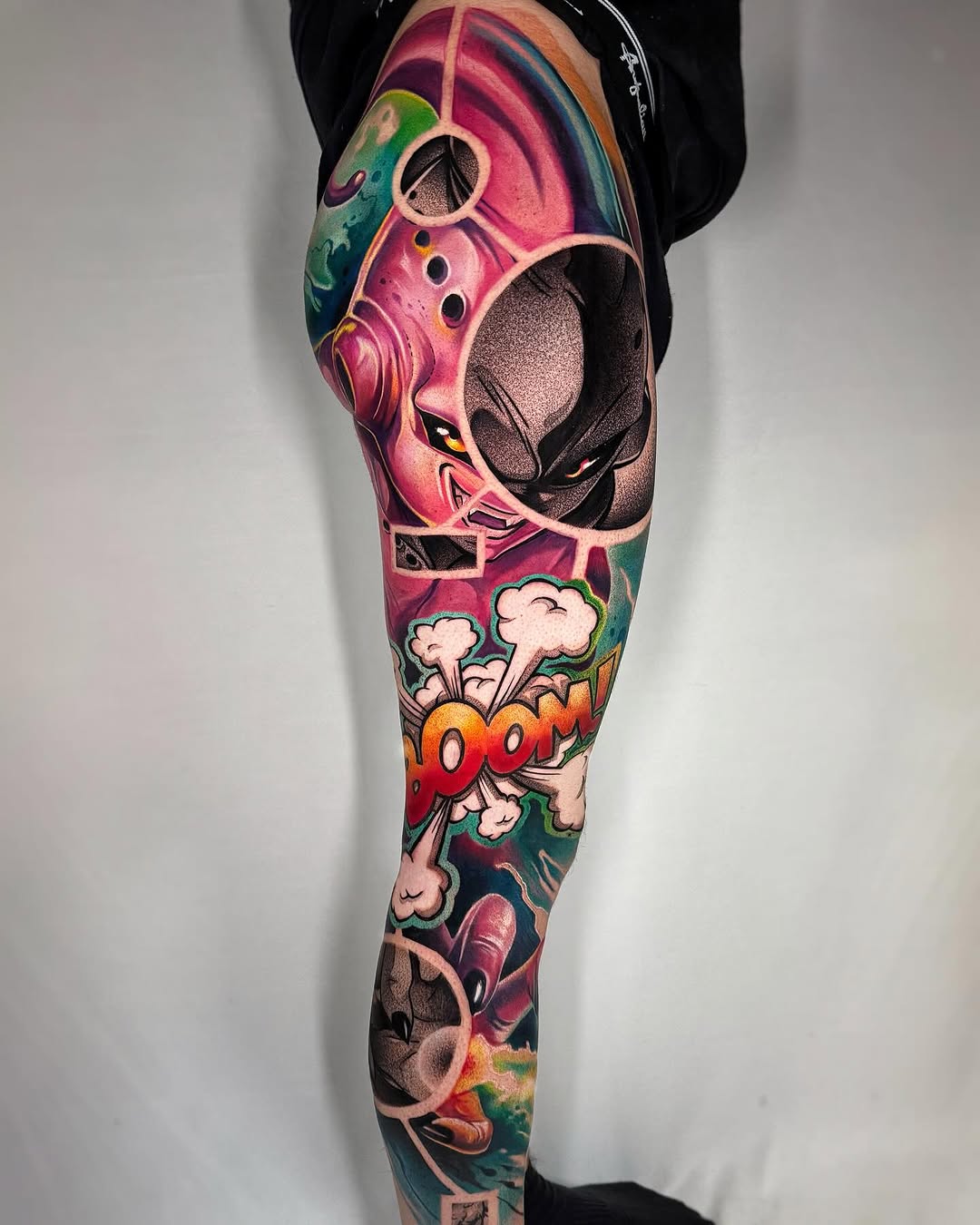 Full leg tattoo featuring a colorful alien head, "BOOM" text, explosion effects, and abstract elements in pink, green, orange, and black.