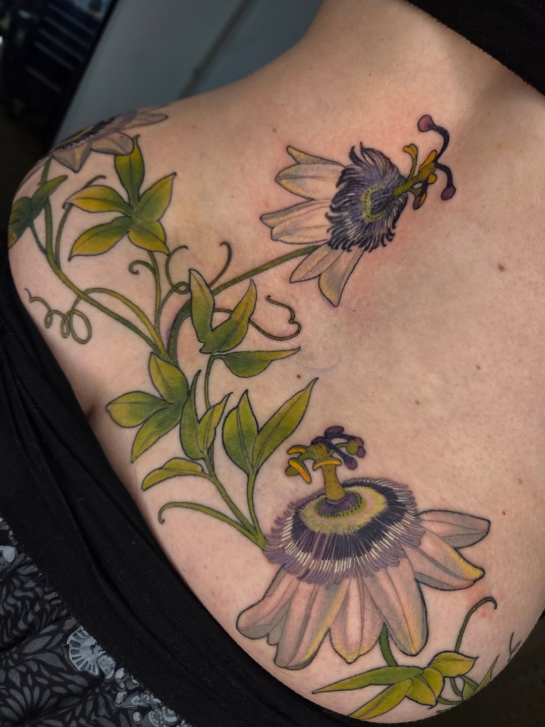 Colorful tattoo on an arm featuring two bees visiting passion flower vines with green leaves and purple-centered blooms.