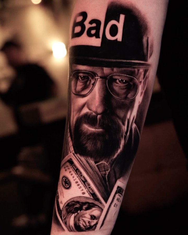 Portrait tattoo on forearm featuring a bearded man with glasses, dollar bill, and "Bald" text above, rendered in black ink.