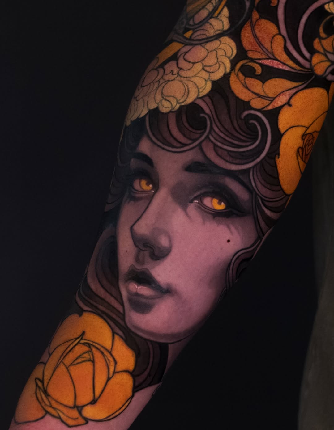 Portrait tattoo of a figure with purple skin, golden eyes, ornate golden headdress and floral elements, displayed on shoulder and arm against dark background.