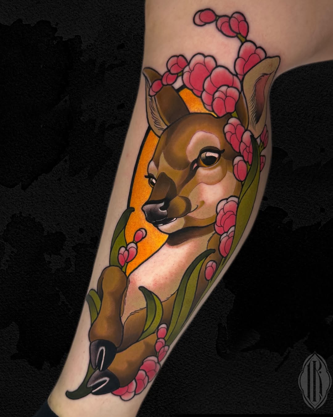 Deer head portrait surrounded by pink flowering branches on the forearm, rendered in brown, pink, orange, and green colors.