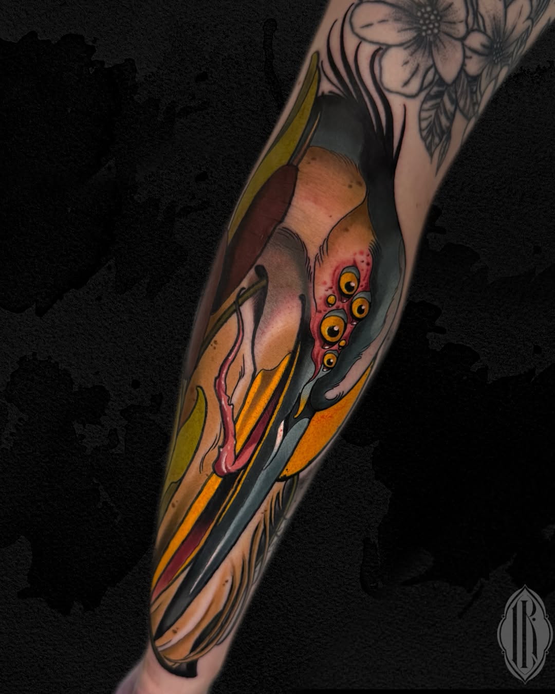 Colorful arm tattoo featuring a surreal face with multiple golden eyes on the inner forearm, surrounded by flowing yellow and orange stripes and decorative elements.