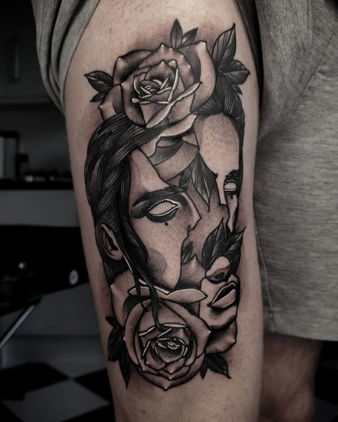 Tattoo on thigh featuring an abstract face with closed eyes, long hair, and roses integrated into the design in black ink on skin.