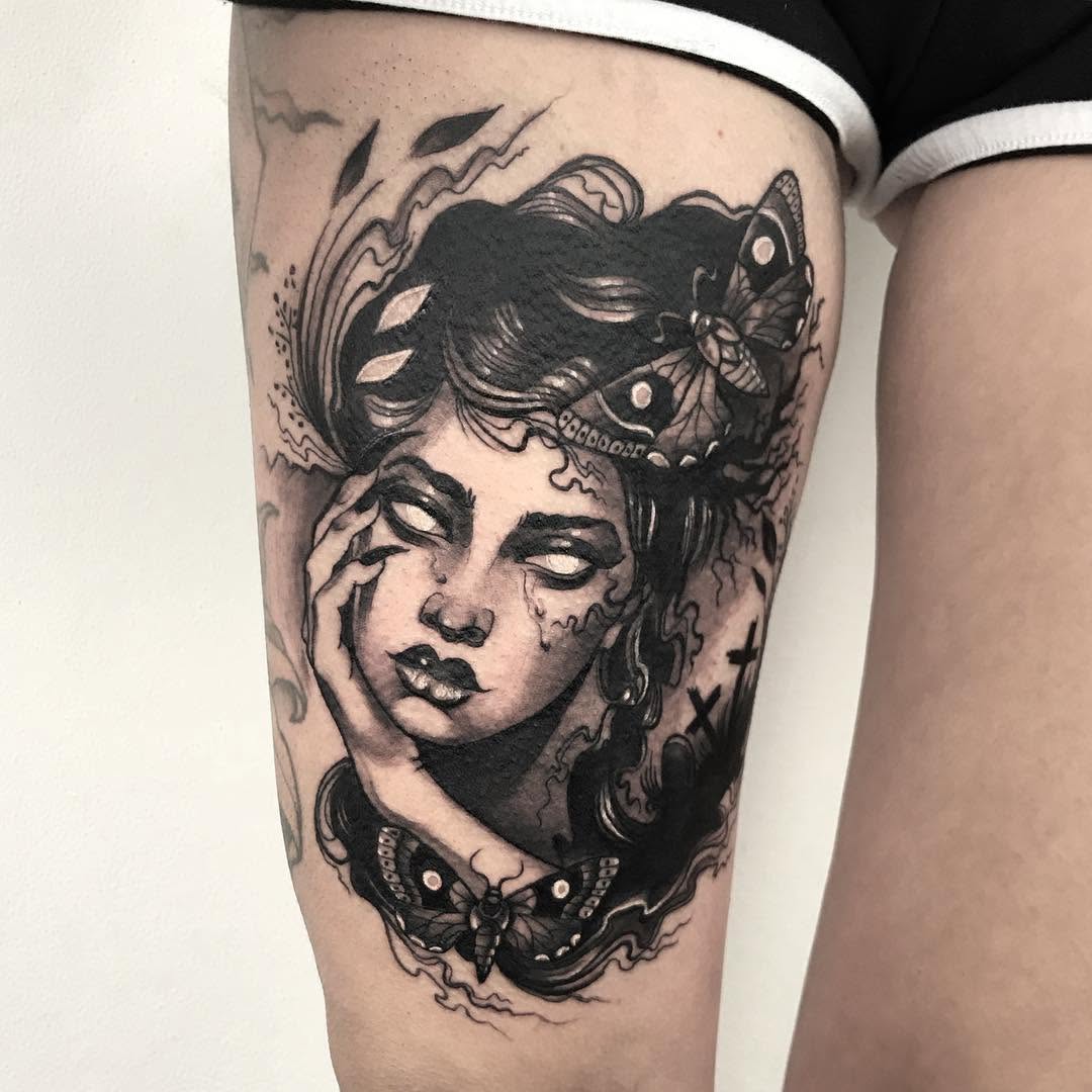 Portrait tattoo on thigh of a woman's face with closed eyes, surrounded by butterflies and decorative swirling elements in black ink.