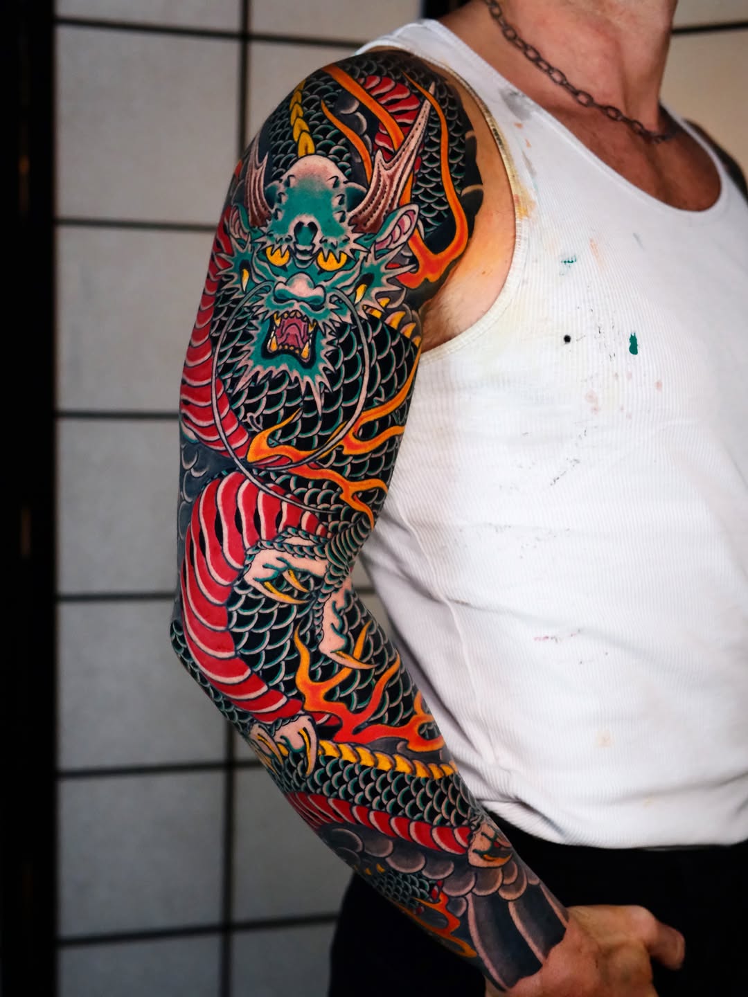 Colorful dragon sleeve tattoo wrapping around the arm from shoulder to wrist, featuring vibrant red, orange, teal, and black scales with detailed facial features.