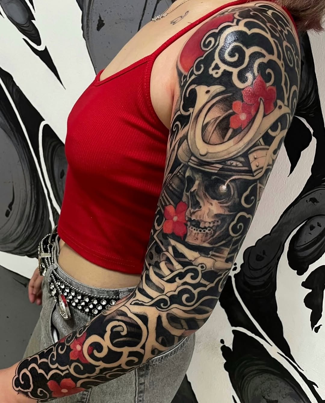 Full sleeve tattoo featuring a skull with decorative scrollwork and red floral accents on the upper arm and forearm.