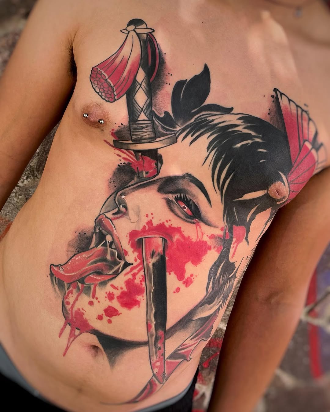 Chest tattoo featuring a demon face with red splatter effects, swords, and flying creatures with pink wings on male torso.