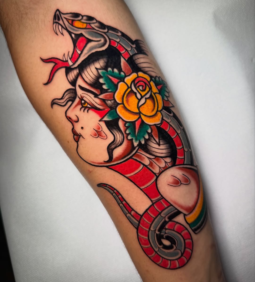 Colorful tattoo on an arm featuring a woman's profile with a serpent and yellow flower, rendered in red, orange, green, and black.