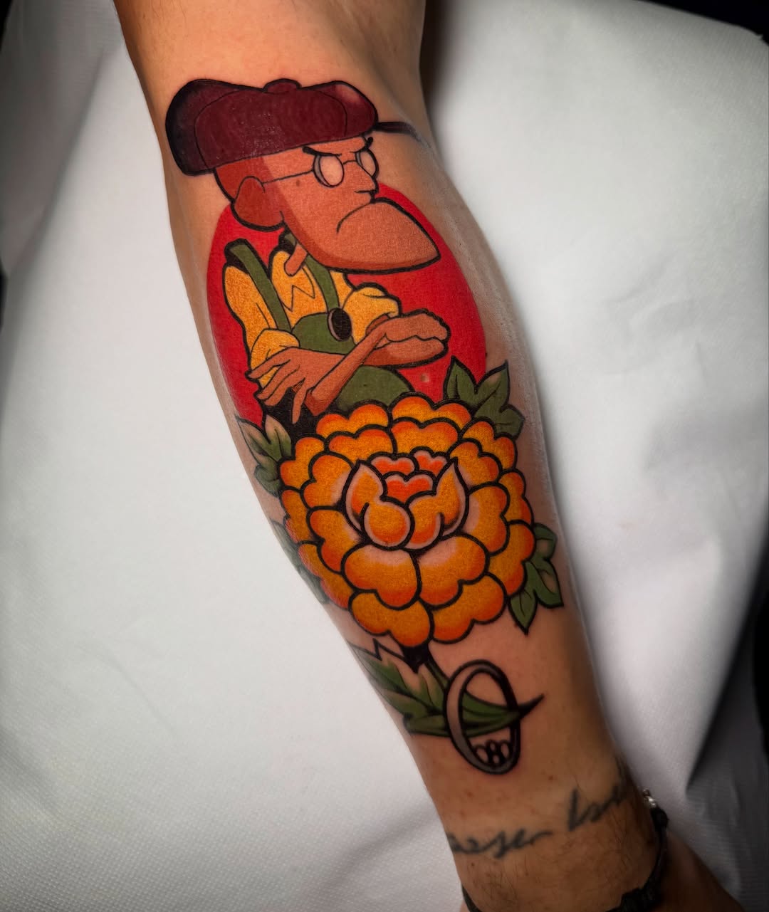 Cartoon character with dark hair and glasses holding a large orange flower on a red background, tattooed on the forearm in bright colors.