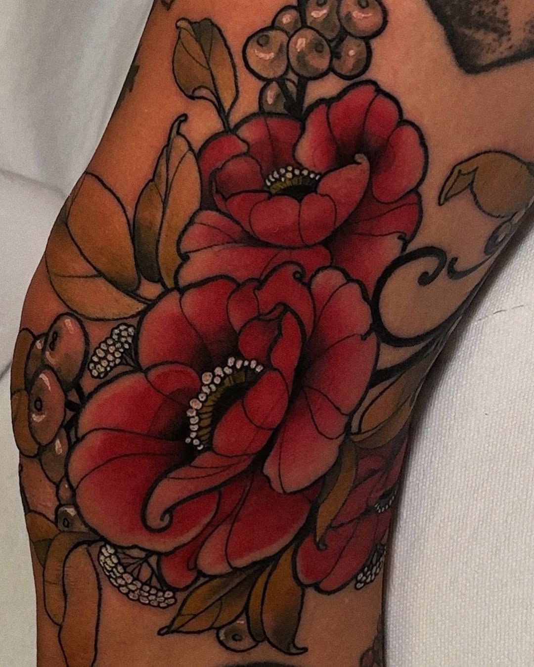 Large red poppies with brown foliage and berries tattooed on the upper arm and shoulder, featuring detailed shading and white highlight details.