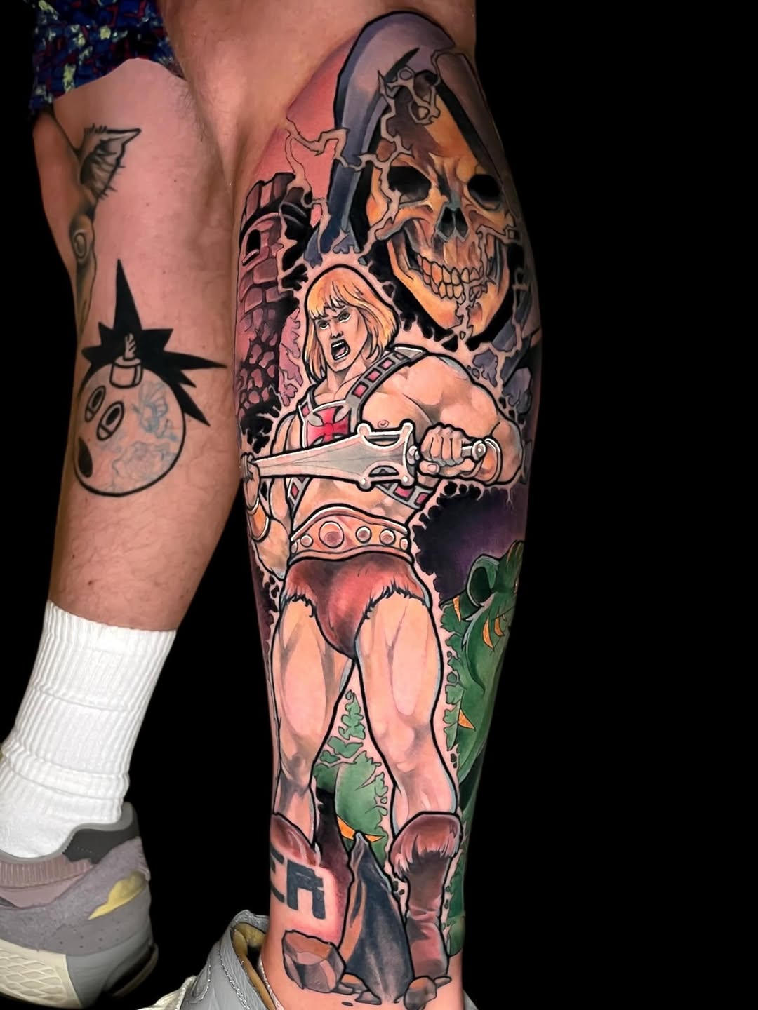 Colorful leg sleeve tattoo featuring a muscular warrior with blonde hair holding an axe, skull imagery, and fantasy creatures in orange, green, and red tones.