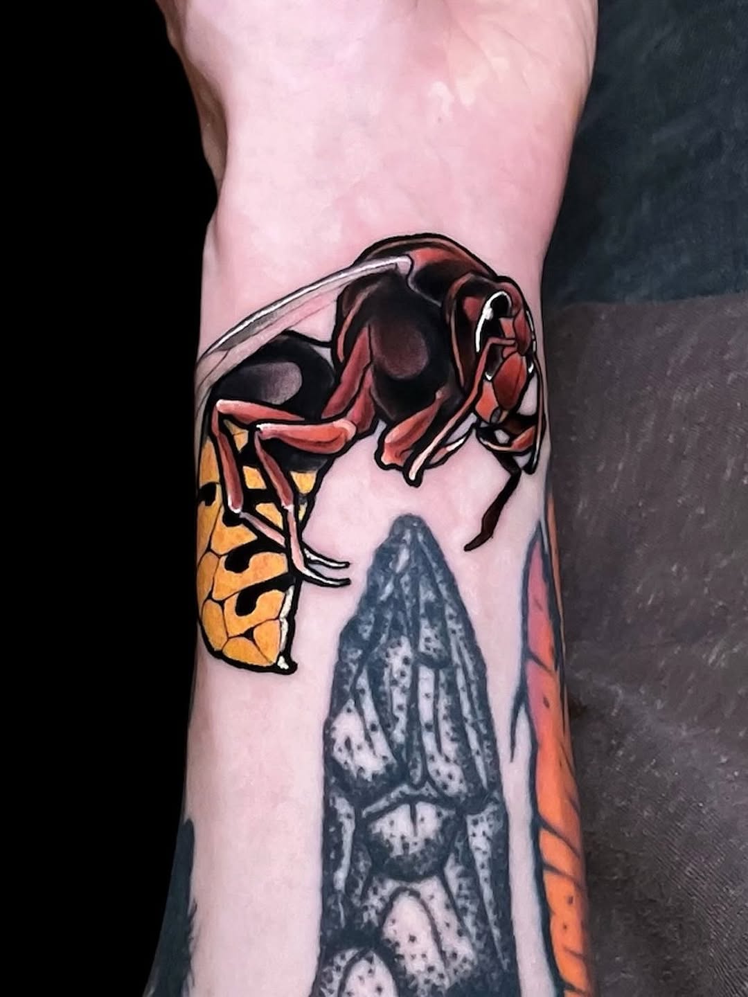 Colorful insect tattoo on forearm featuring a red beetle, yellow and black butterfly, and gray moth with orange accents.