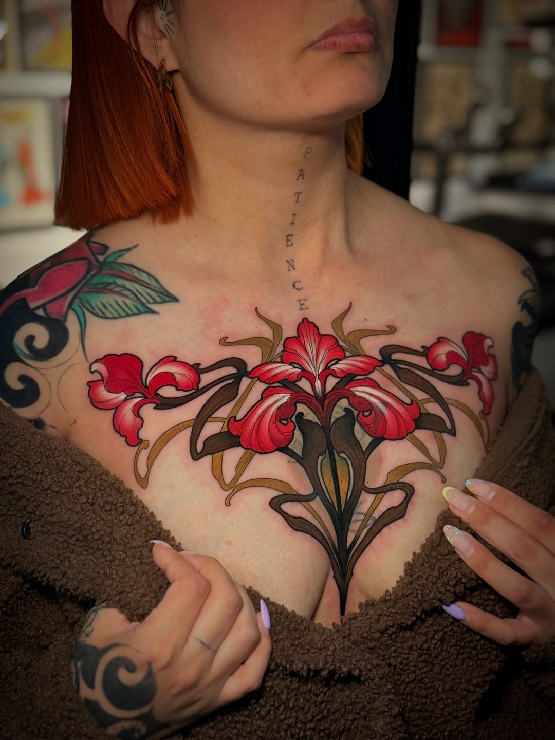 Chest tattoo featuring red iris flowers with brown stems and leaves, with "PATIENCE" lettering running vertically down the neck.