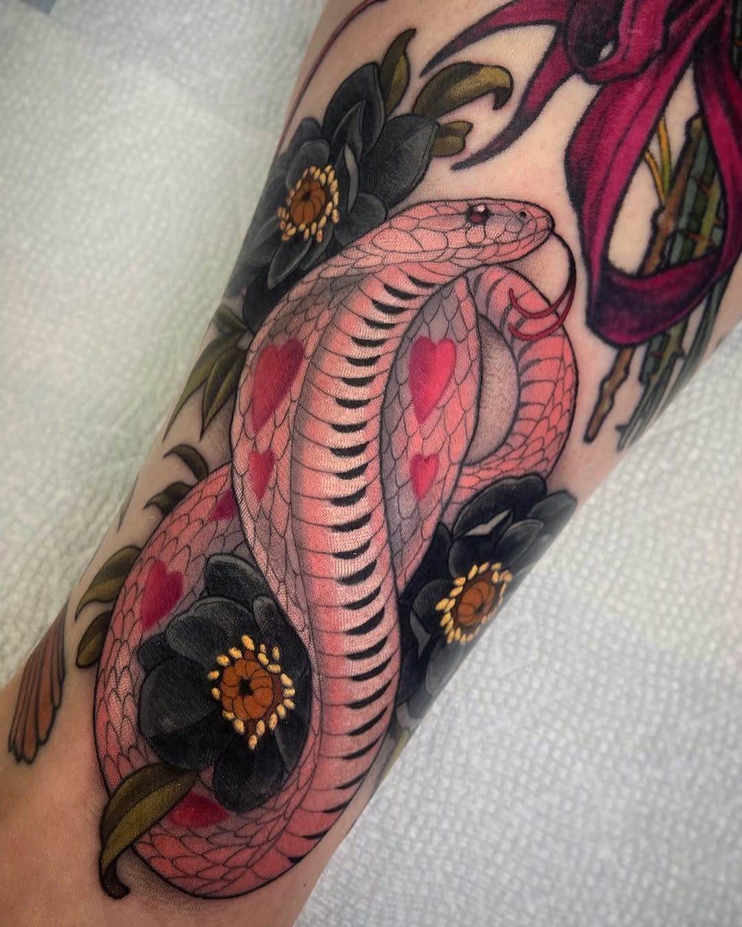 Pink cobra with detailed scales and red markings surrounded by black flowers with golden centers on the upper arm.