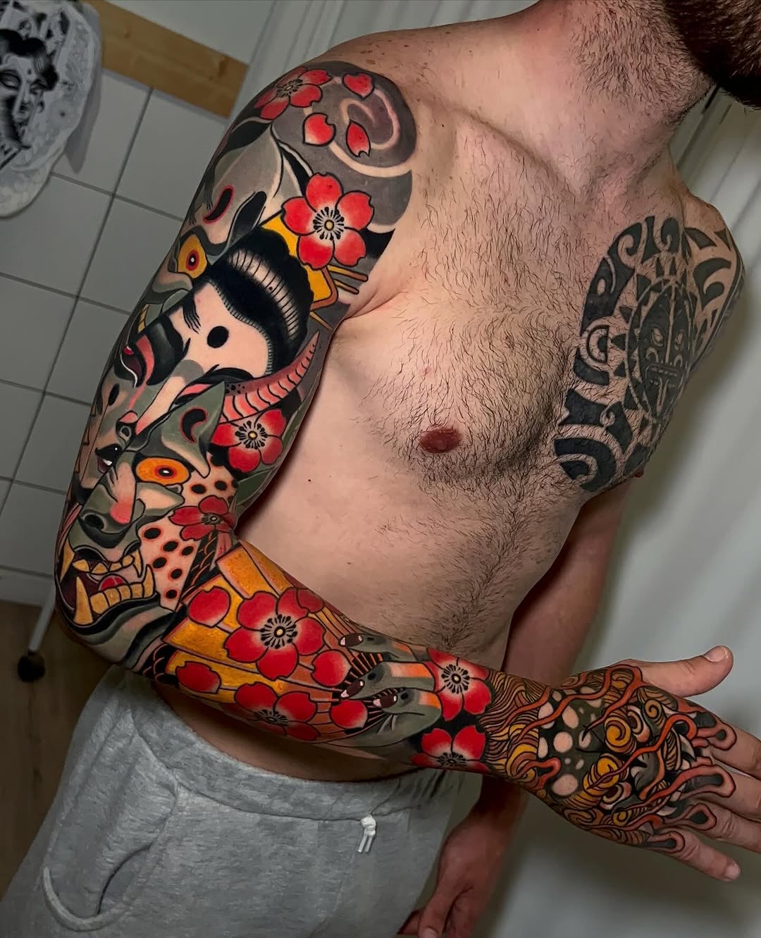 Colorful arm sleeve tattoo featuring stacked skulls with red flowers, orange accents, and decorative patterns extending from shoulder to hand.