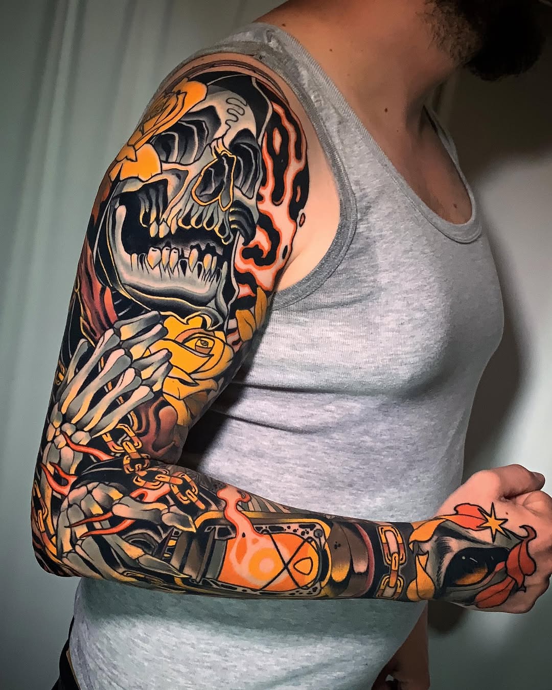 Full sleeve tattoo featuring a flaming skull with skeletal hand, lantern, and decorative elements in orange, red, yellow, and black on the arm and hand.