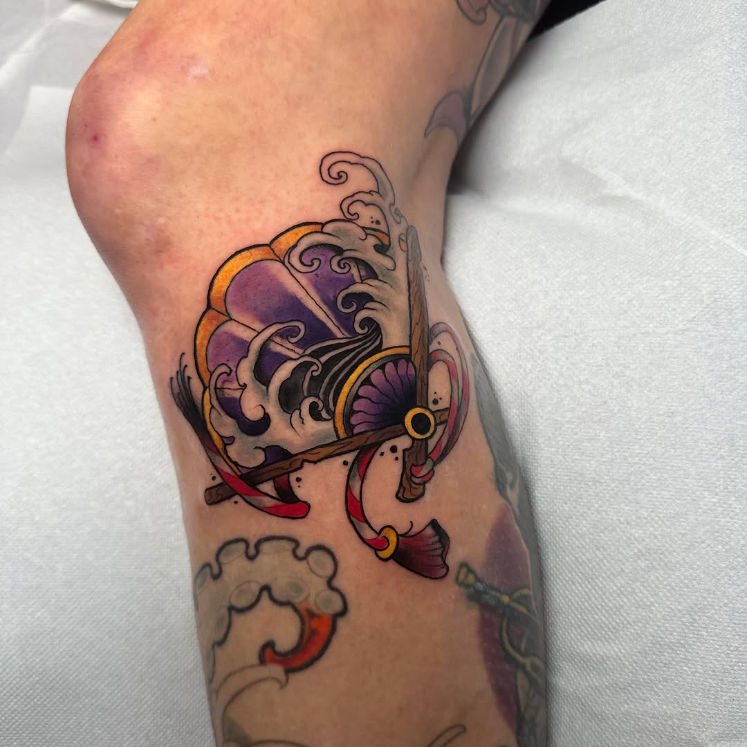 Colorful ornamental tattoo featuring purple and gold shells with decorative scrollwork and red ribbon elements on the calf.