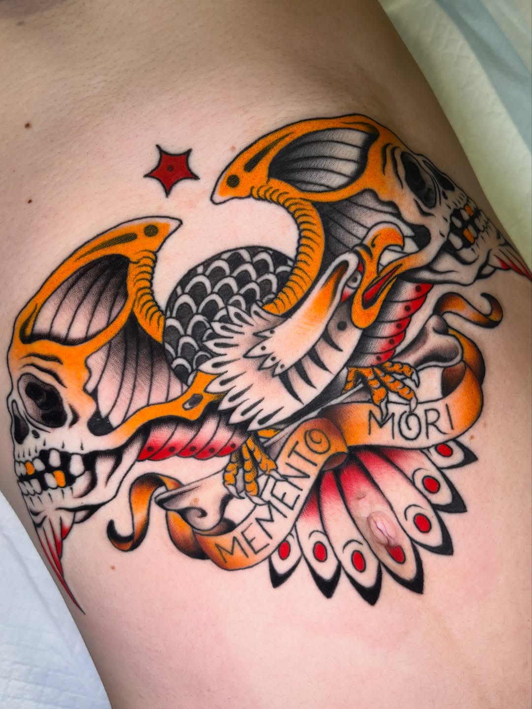 Colorful skull with orange bat wings, red mouth, black scales, and "MEMENTO MORI" text on the upper arm.