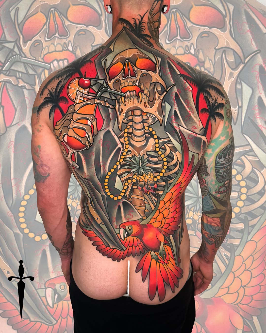 Full back tattoo featuring a skull with skeleton anatomy, birds, beads, and tropical elements in red, orange, yellow, and black colors.