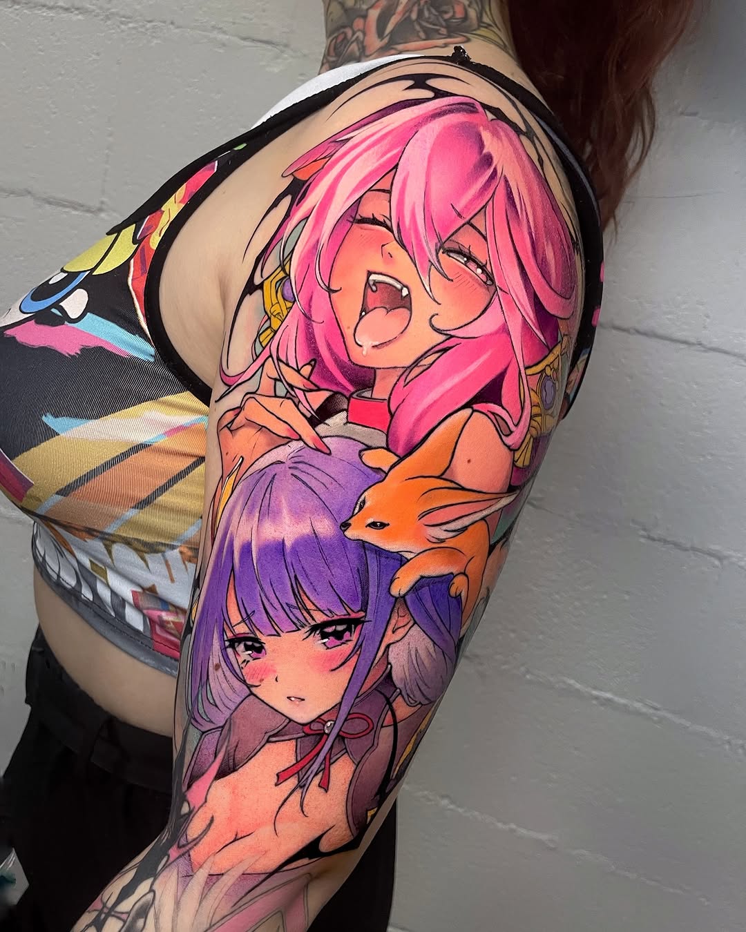 Colorful sleeve tattoo featuring two female characters with pink and purple hair, accompanied by orange foxes, displayed on an arm against a brick wall.