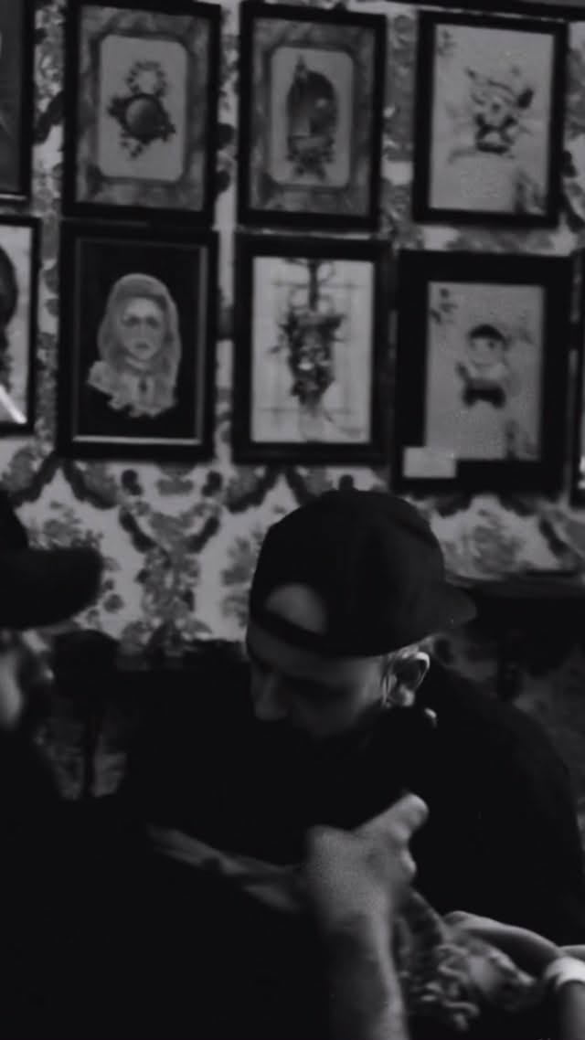 Person wearing dark clothing displays six framed portrait drawings on a wall, featuring various faces and decorative elements in black and white.