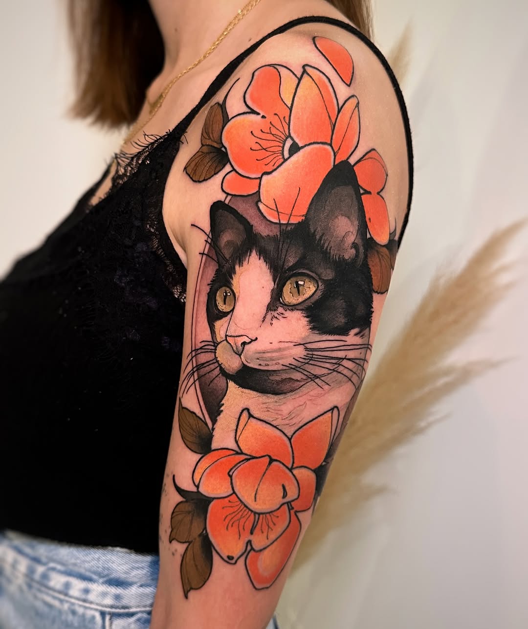 Black and white cat with golden eyes surrounded by orange and red flowers on the upper arm.