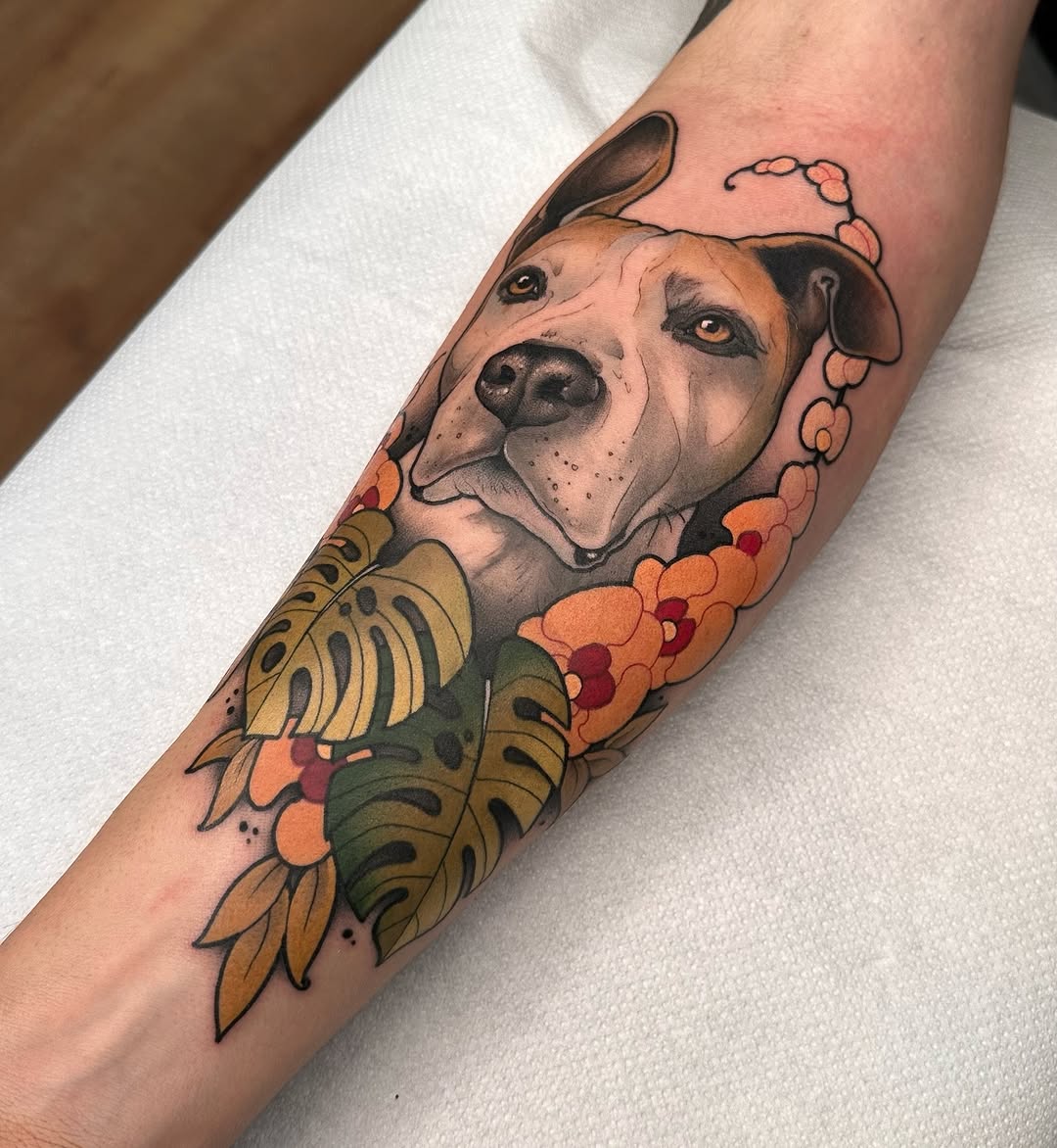 Dog portrait tattoo on forearm featuring a tan and white dog's head surrounded by orange flowers, green leaves, and decorative beading in warm earth tones.
