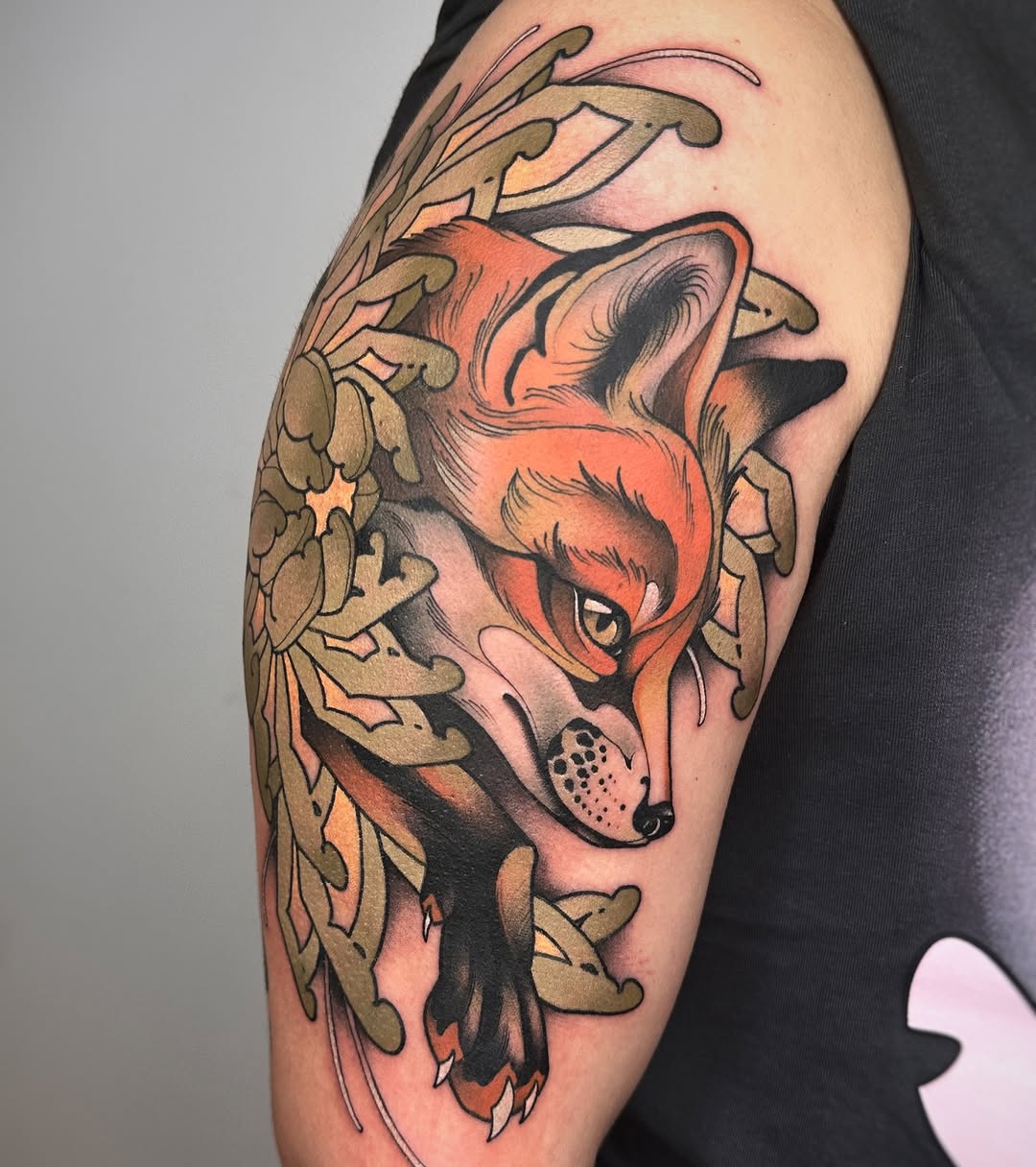 Colorful fox head tattoo with ornamental antlers and decorative foliage in orange, tan, and black on the upper arm.