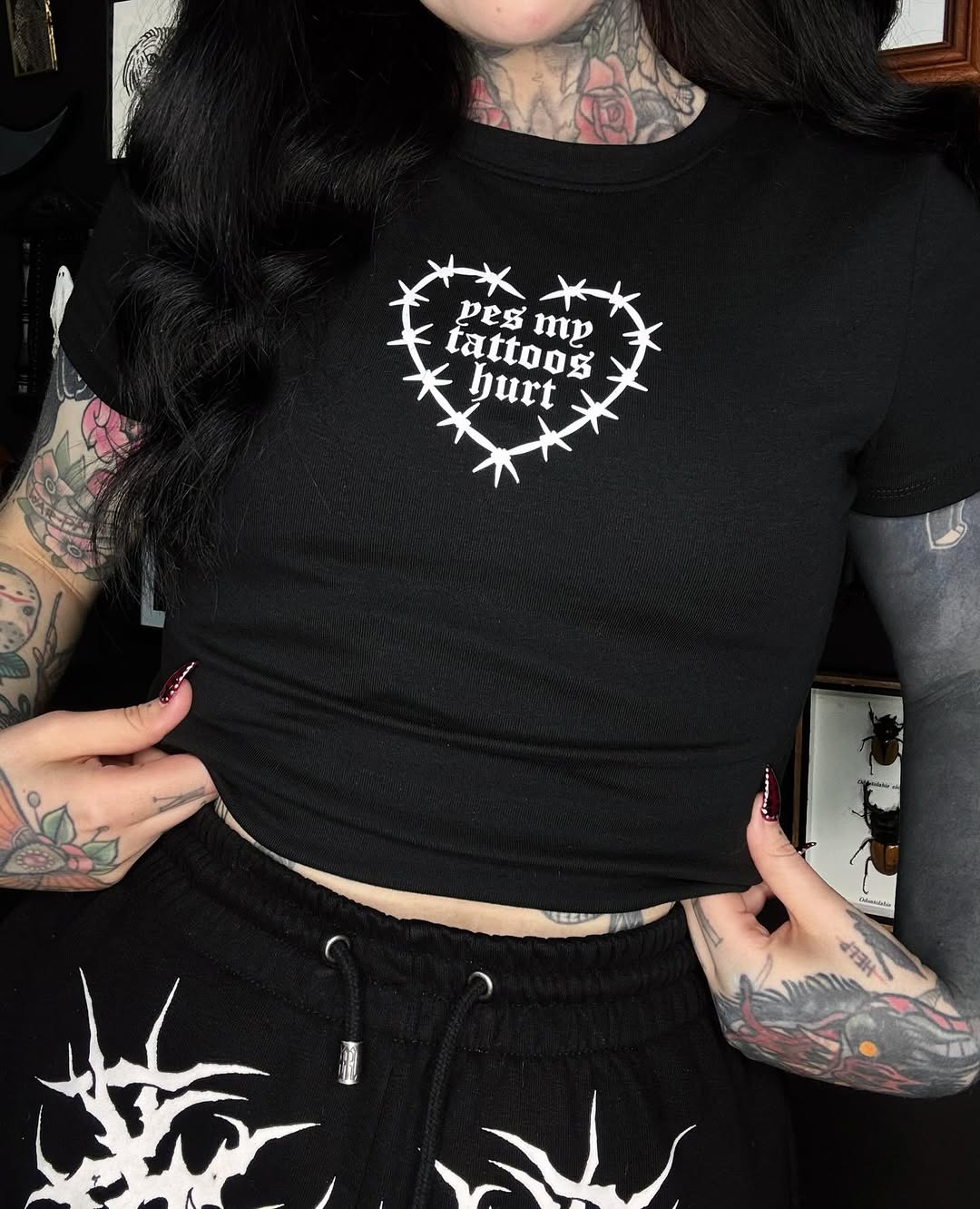 Person wearing black clothing displaying multiple colored tattoos on neck, arms, and hands, including floral designs and geometric patterns.