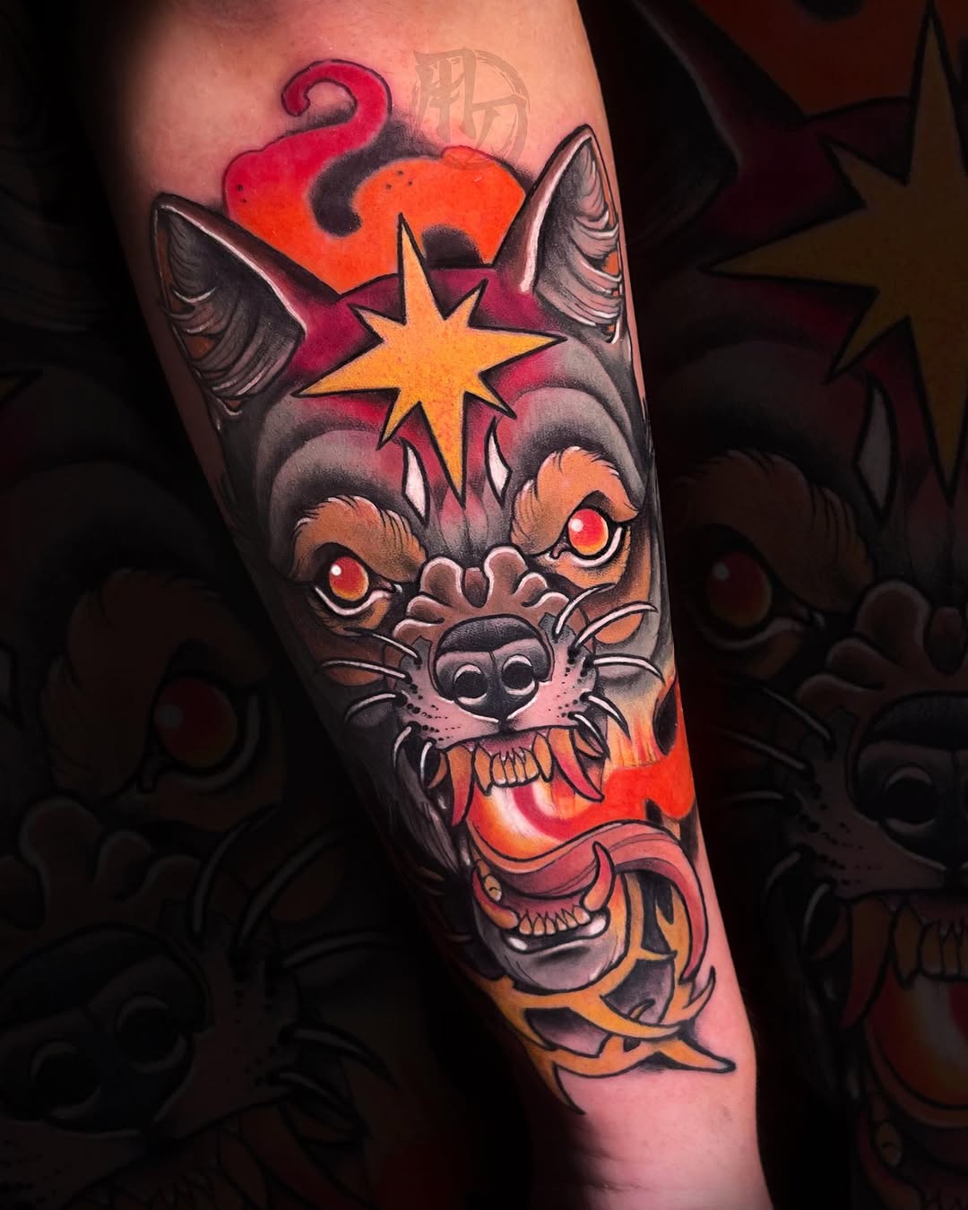A colorful cat head tattoo with glowing eyes, star, flames, and skull elements in red, orange, and black on the forearm.