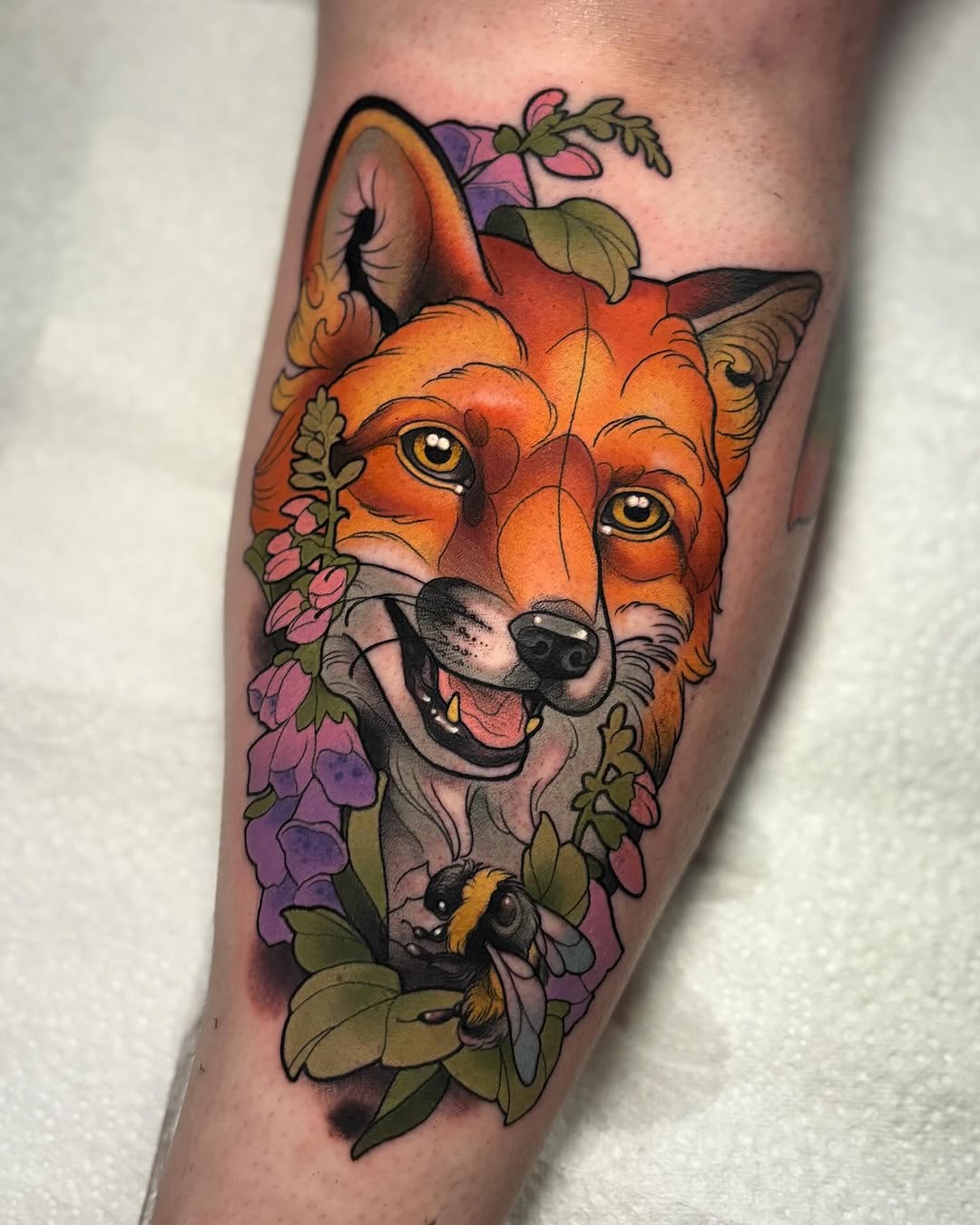 Colorful fox head tattoo with golden eyes surrounded by pink and purple flowers on the calf, featuring a small bee at the bottom.