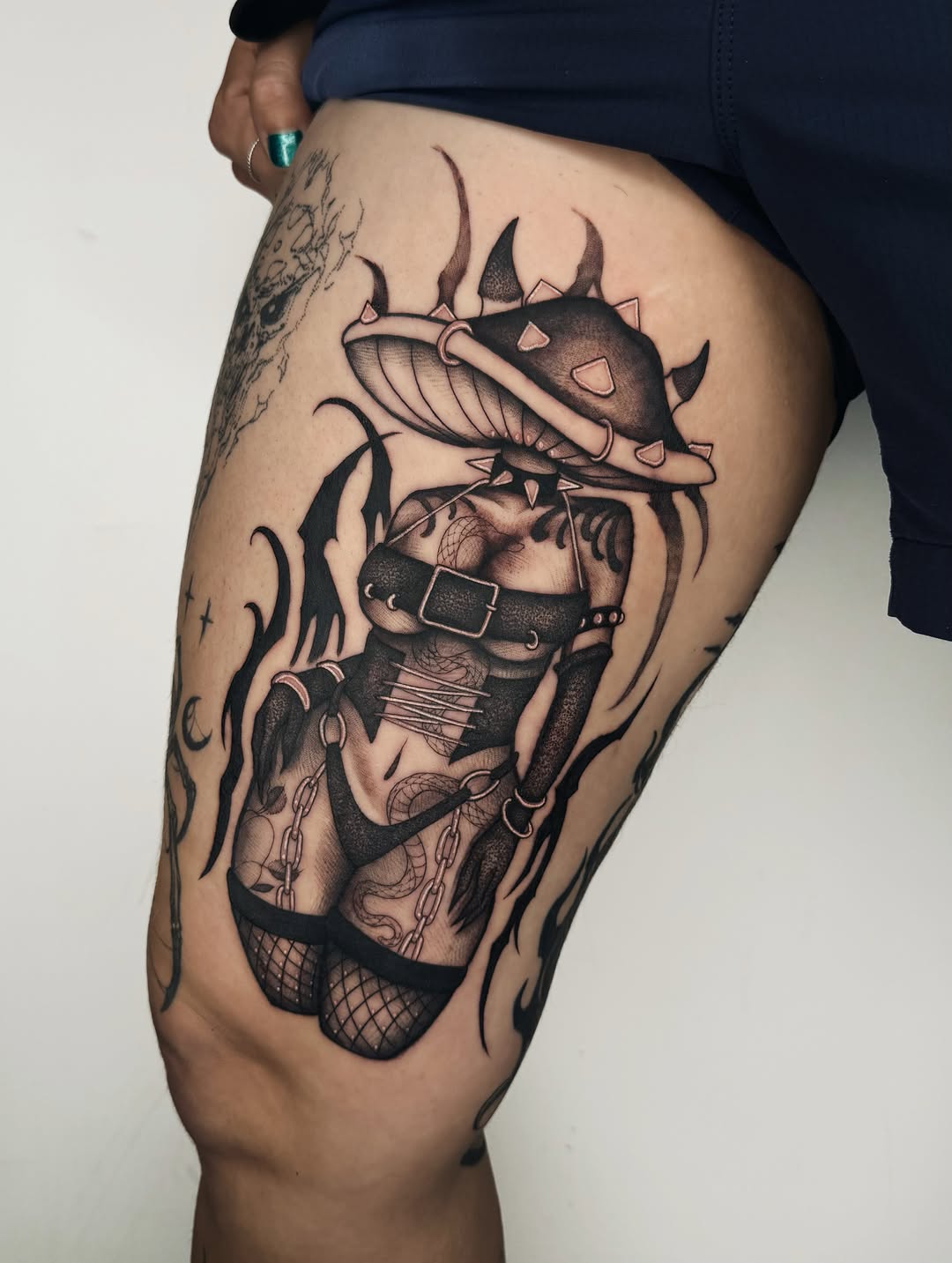 Demonic creature tattoo on thigh featuring horned beast with bound figure, rendered in black ink with gray shading on human leg.