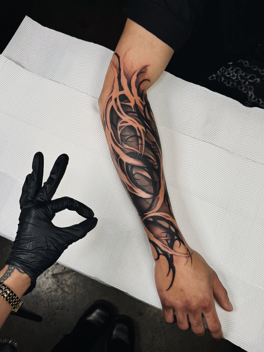 Tribal and organic patterned tattoo covering the forearm and hand in black and brown ink on light skin tone.