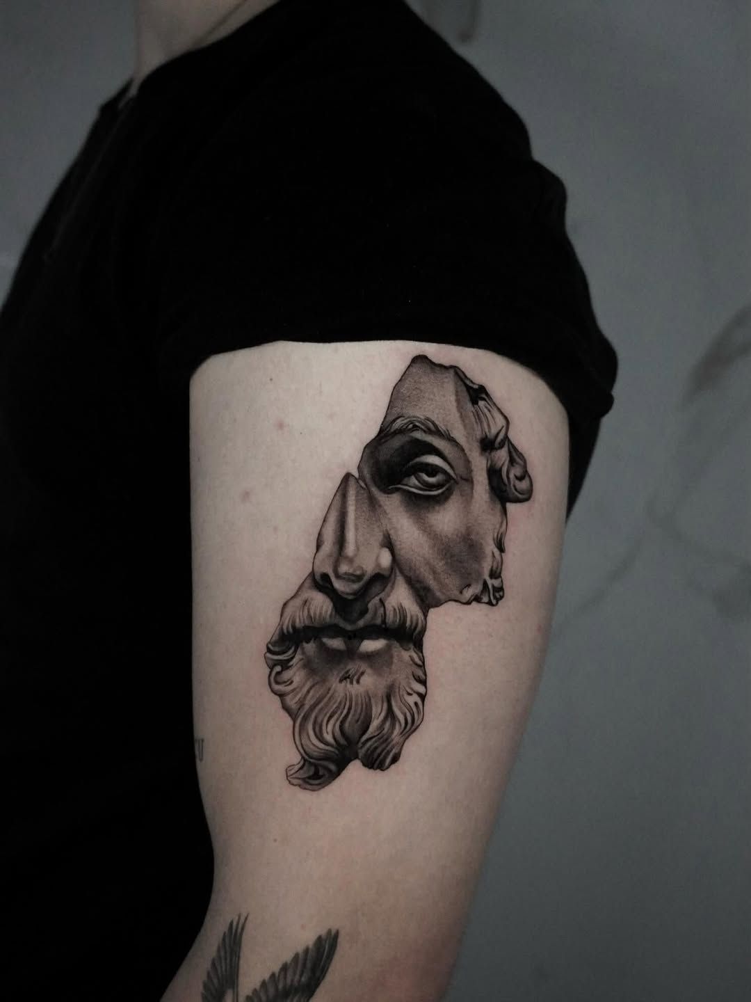 Monochrome portrait tattoo on upper arm showing a bearded man's face in profile with detailed shading and linework.