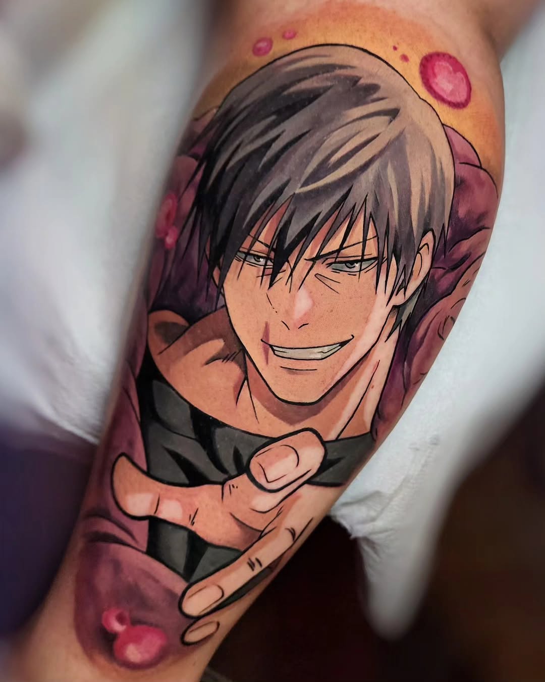 Anime character portrait tattoo on upper arm featuring a smiling male face with dark hair, rendered in color with purple and pink background elements.