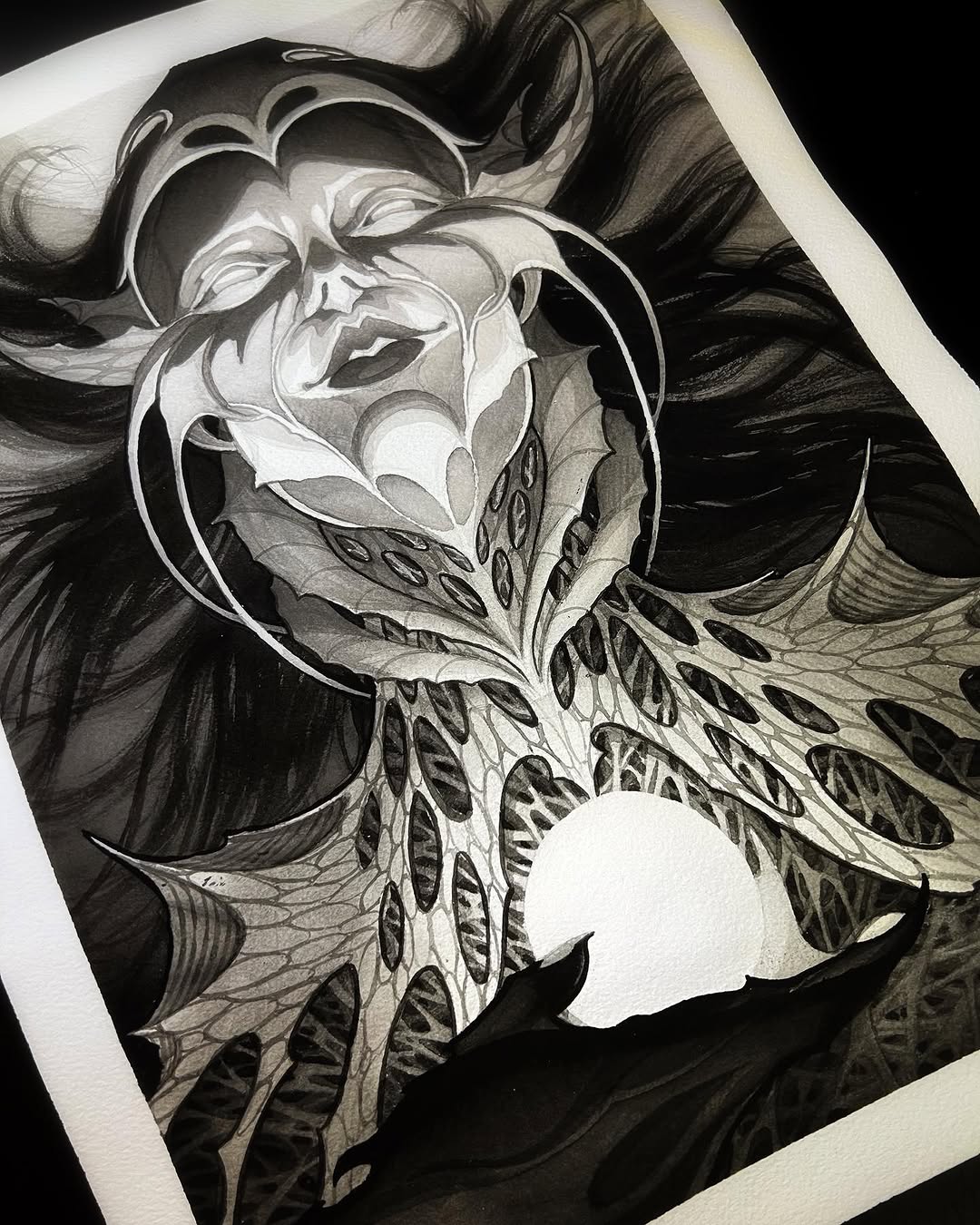 Detailed skull with flowing hair and ornate wing patterns rendered in black ink and grayscale on white paper.