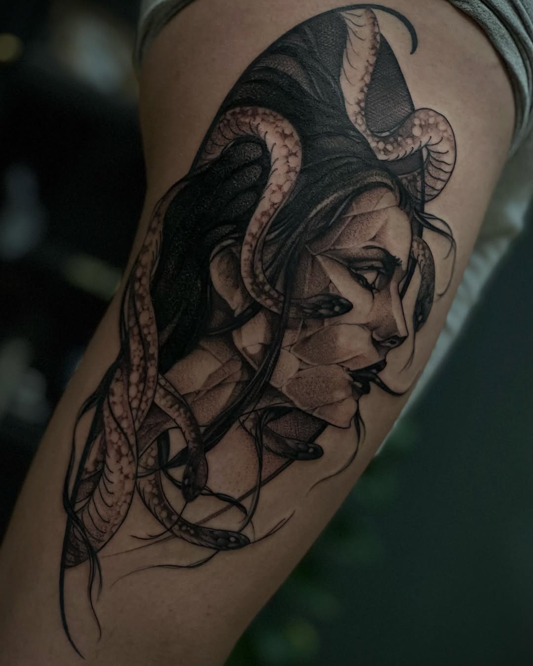 Profile of a woman's face with serpents wrapping around her head and neck, rendered in black and brown ink on the upper arm.