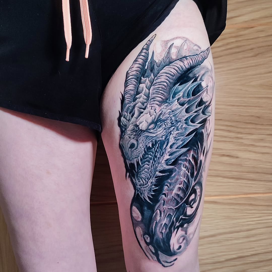 Detailed demon head with curved horns and scales tattooed on thigh in black and gray ink with purple shading.