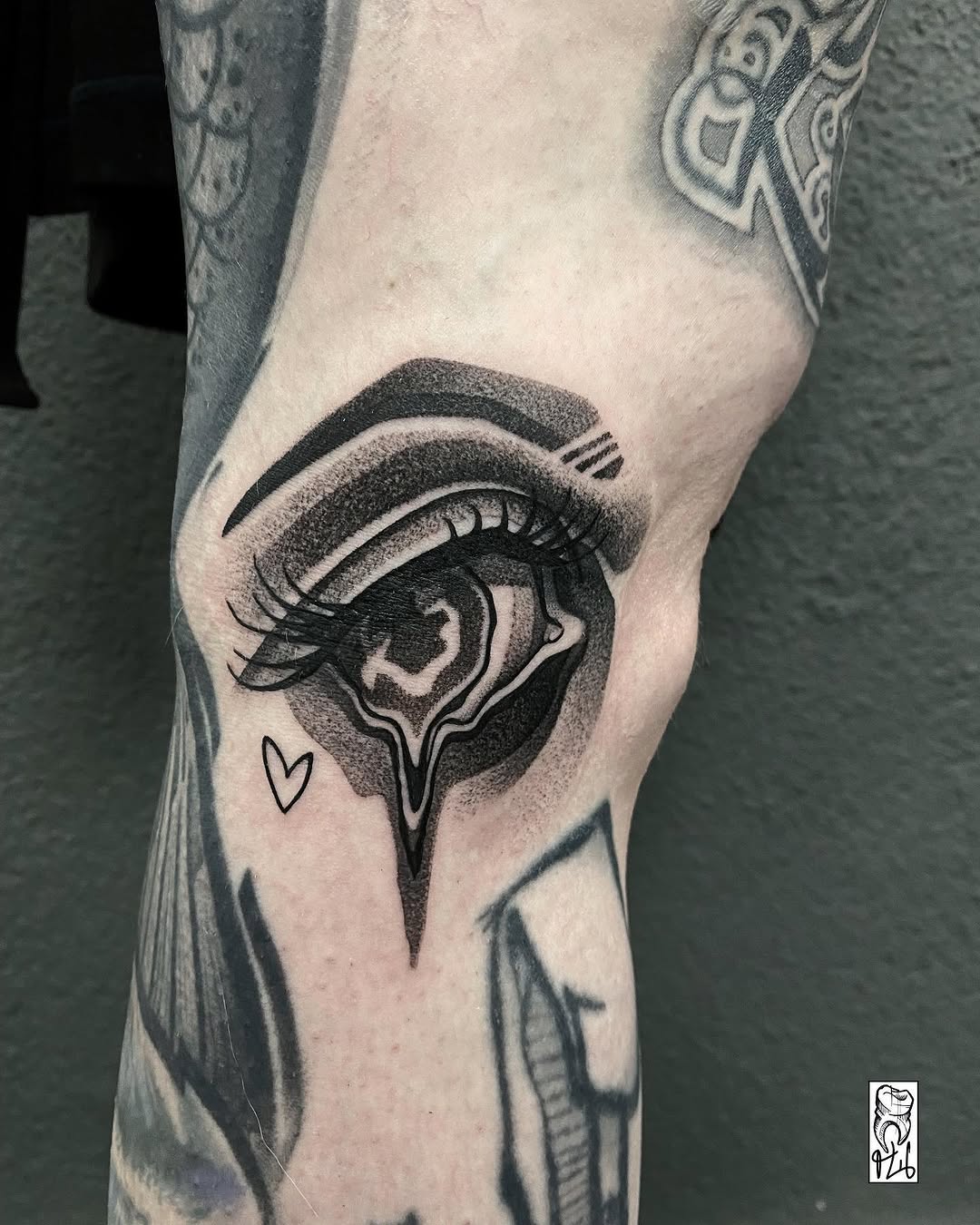 Detailed eye tattoo on knee with curved eyebrow, long lashes, decorative iris, and small heart, rendered in black ink.
