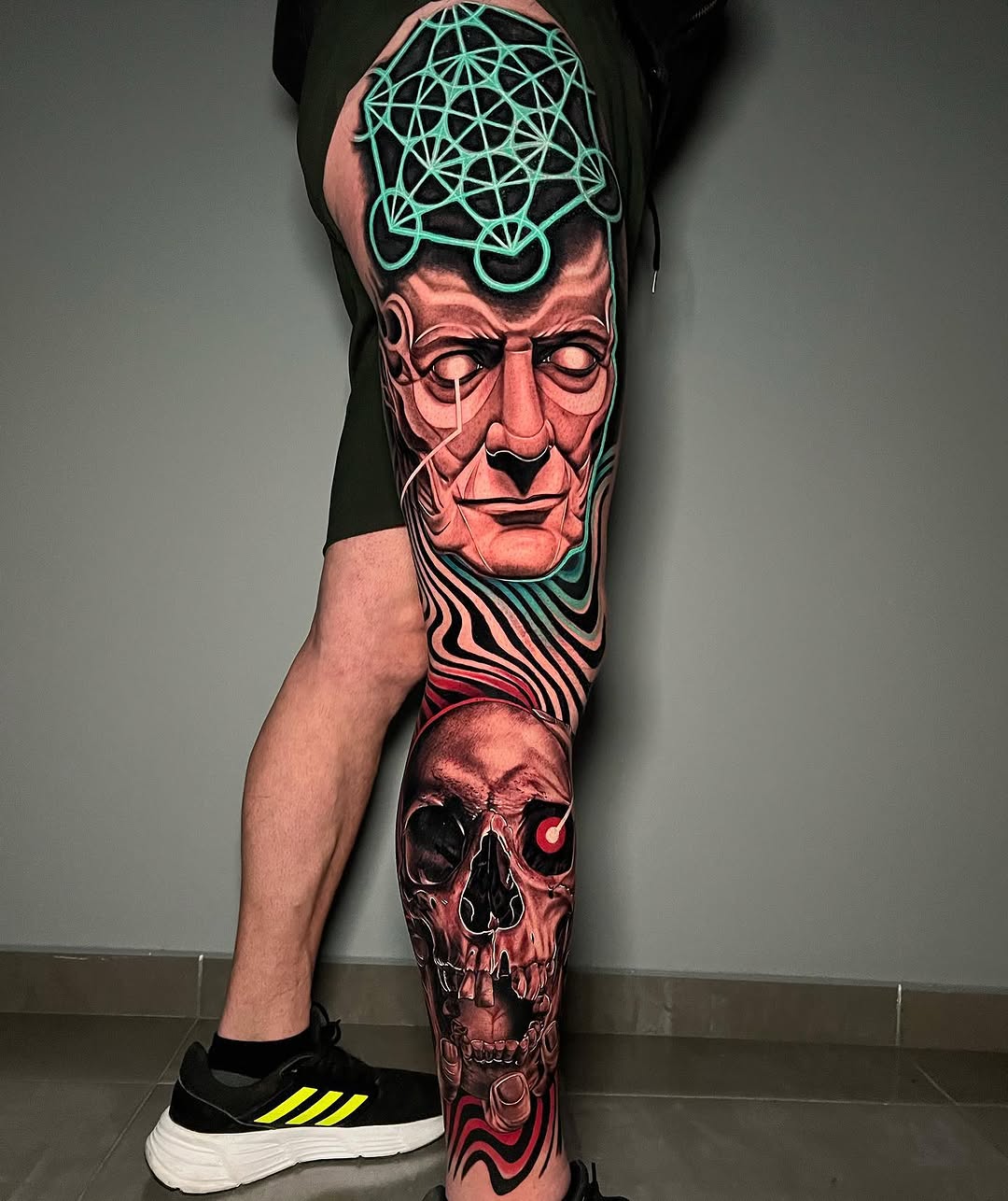 Full-leg tattoo sleeve featuring a geometric-patterned head at the thigh, wavy lines at mid-leg, and a skull with red accents at the calf, in red, black, and neon green.