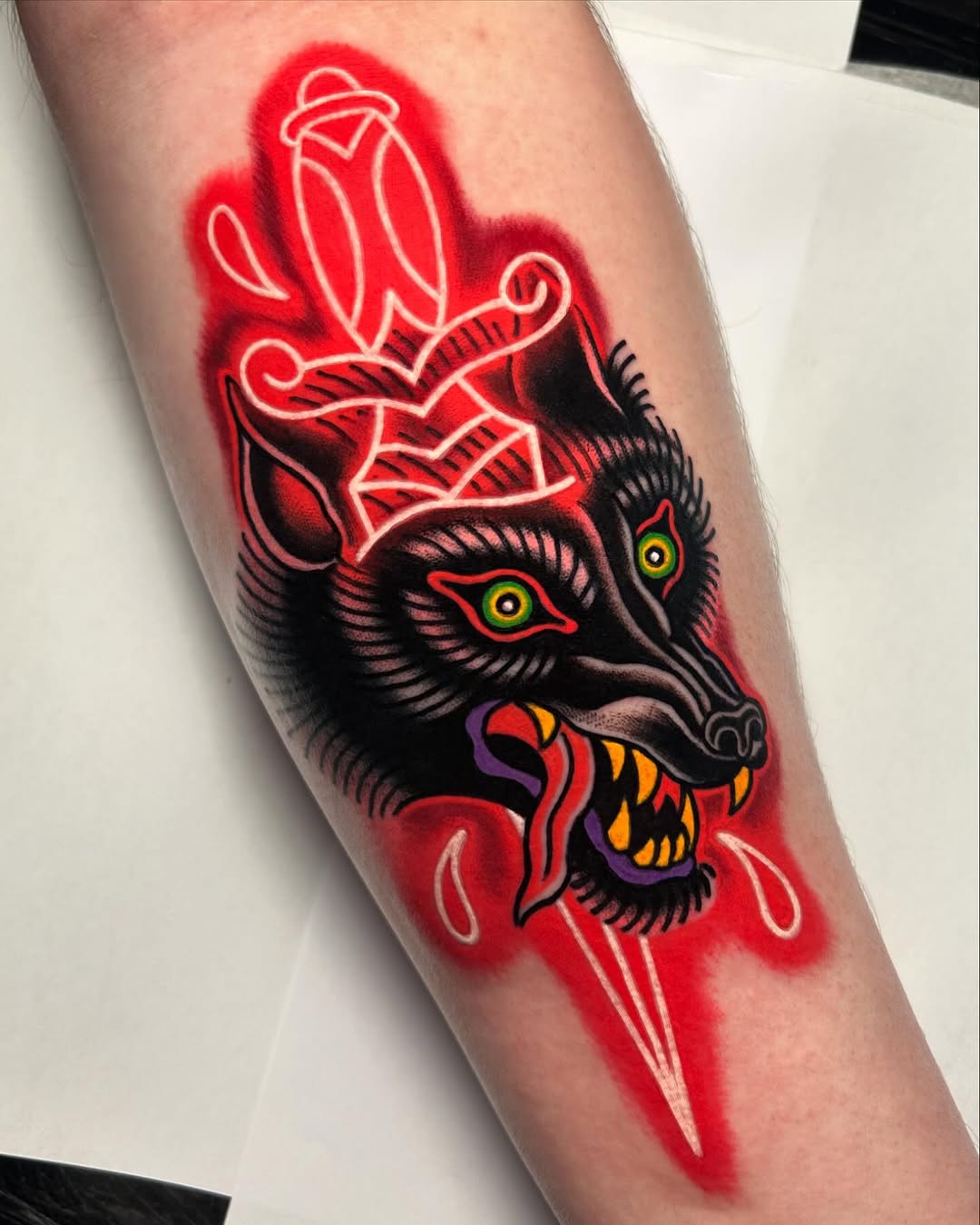 Vibrant red neon-glowing wolf head with yellow eyes and colorful mouth design on forearm, surrounded by ornamental sword and leaf motifs.