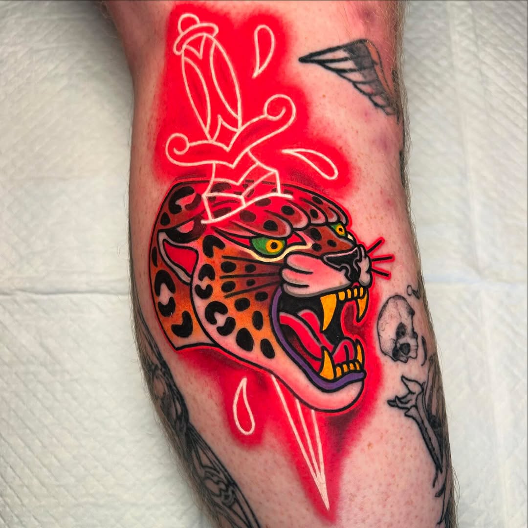 Colorful leopard head tattoo with red neon glow effect and decorative leaf designs on upper arm, featuring green eyes and yellow accents.