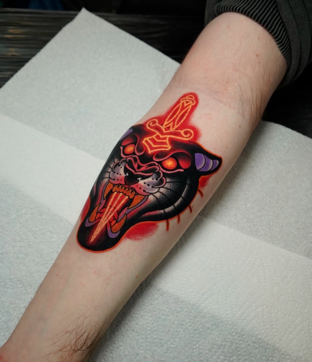 A vibrant red and orange demonic creature with glowing neon accents and purple horns tattooed on the forearm, featuring intricate line work and color gradients.