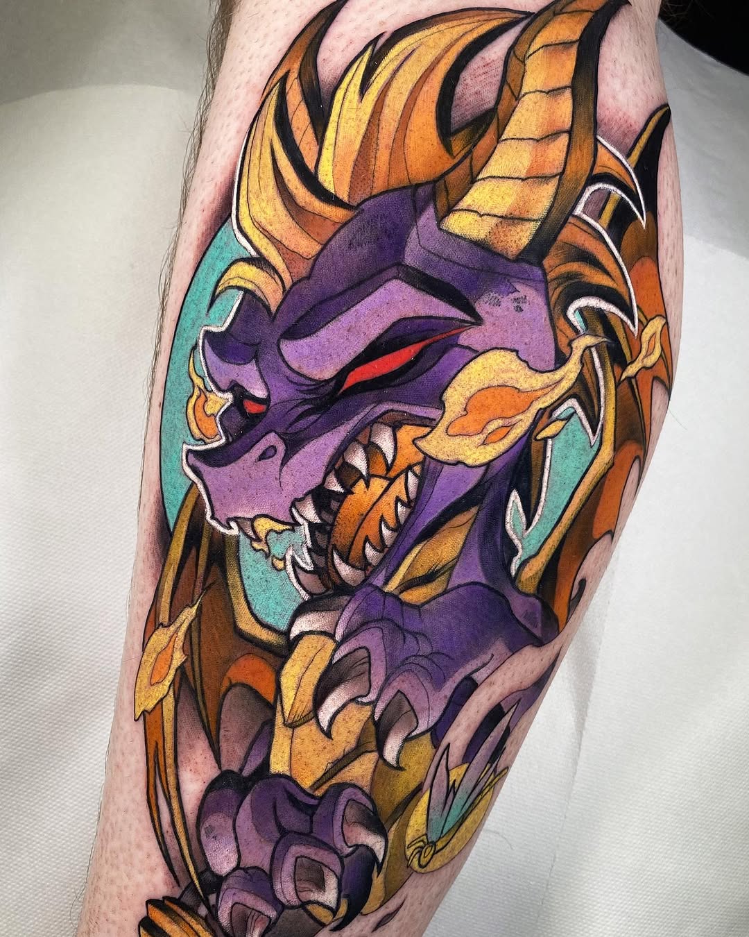 Colorful demon mask tattoo with purple face, golden horns, orange and yellow details, and turquoise background on the calf.