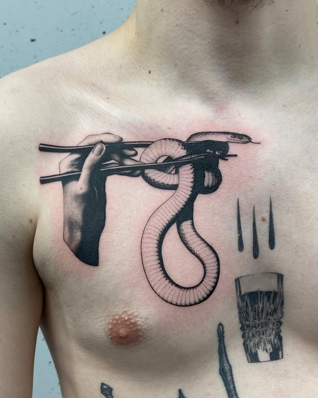 Chest tattoo depicting a hand holding chopsticks with a snake and small fish, rendered in black ink with fine detail work.