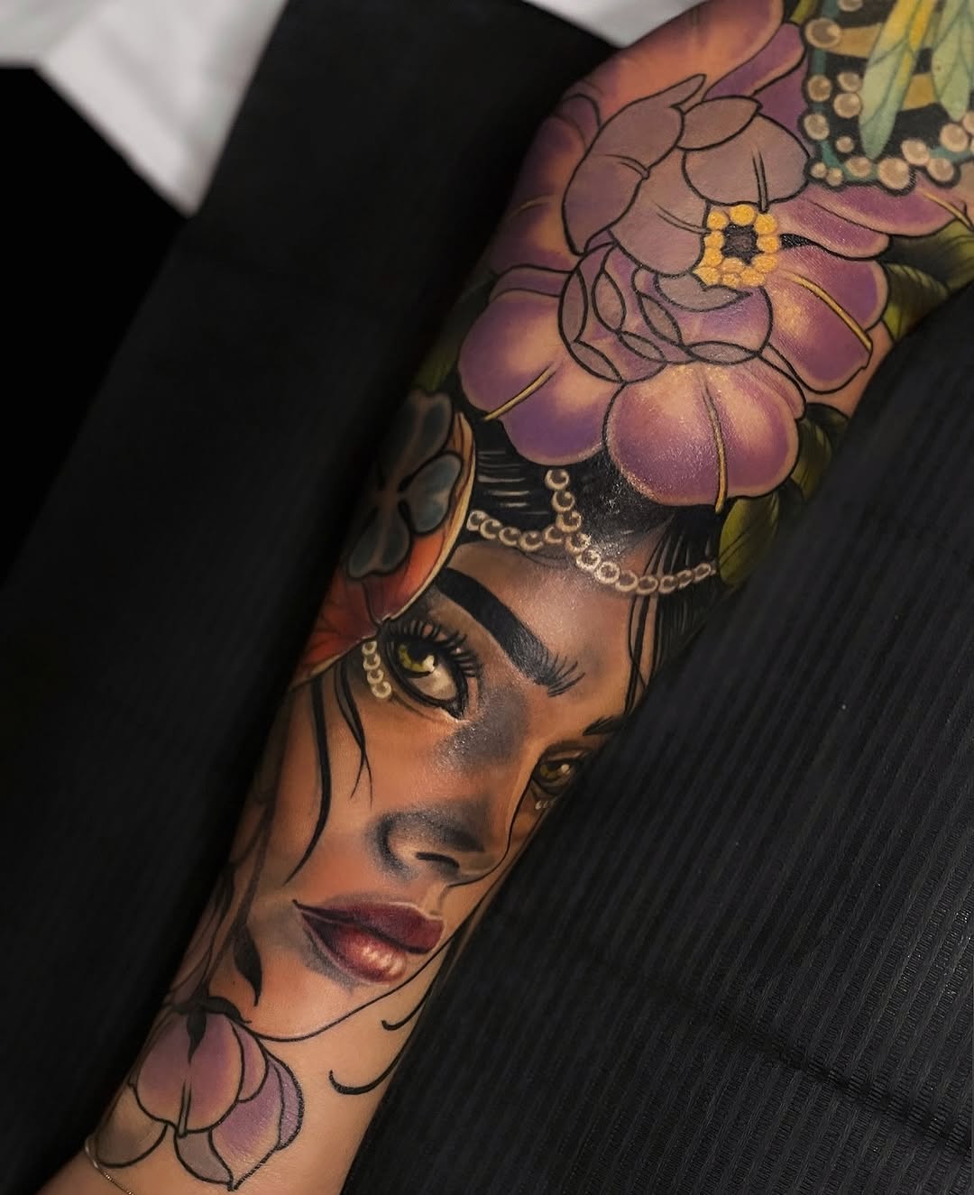 Woman's forearm tattoo featuring a female face with flowers in her hair, rendered in purple, pink, yellow, and black colors.