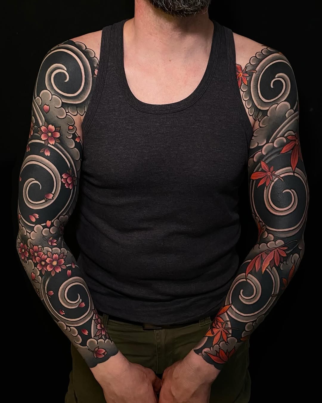 Symmetrical full sleeve tattoos featuring large spiral designs, red and pink flowers, and ornamental scrollwork on a shirtless man's arms.