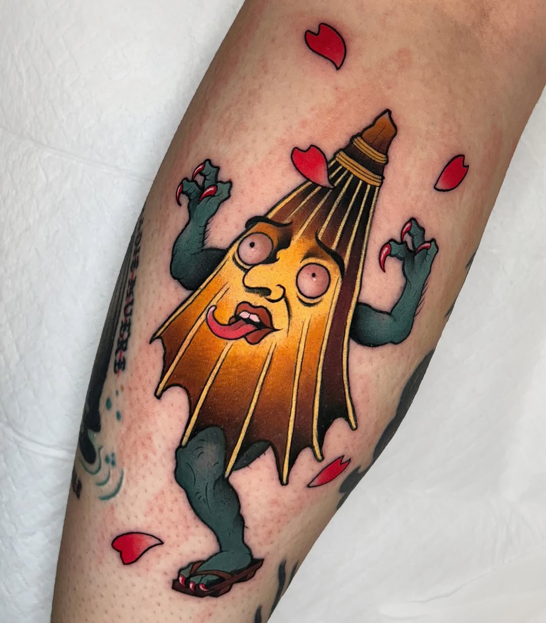 Colorful tattoo on a forearm featuring a yellow anthropomorphic banana character with green zombie hands surrounded by red hearts and green rose designs.