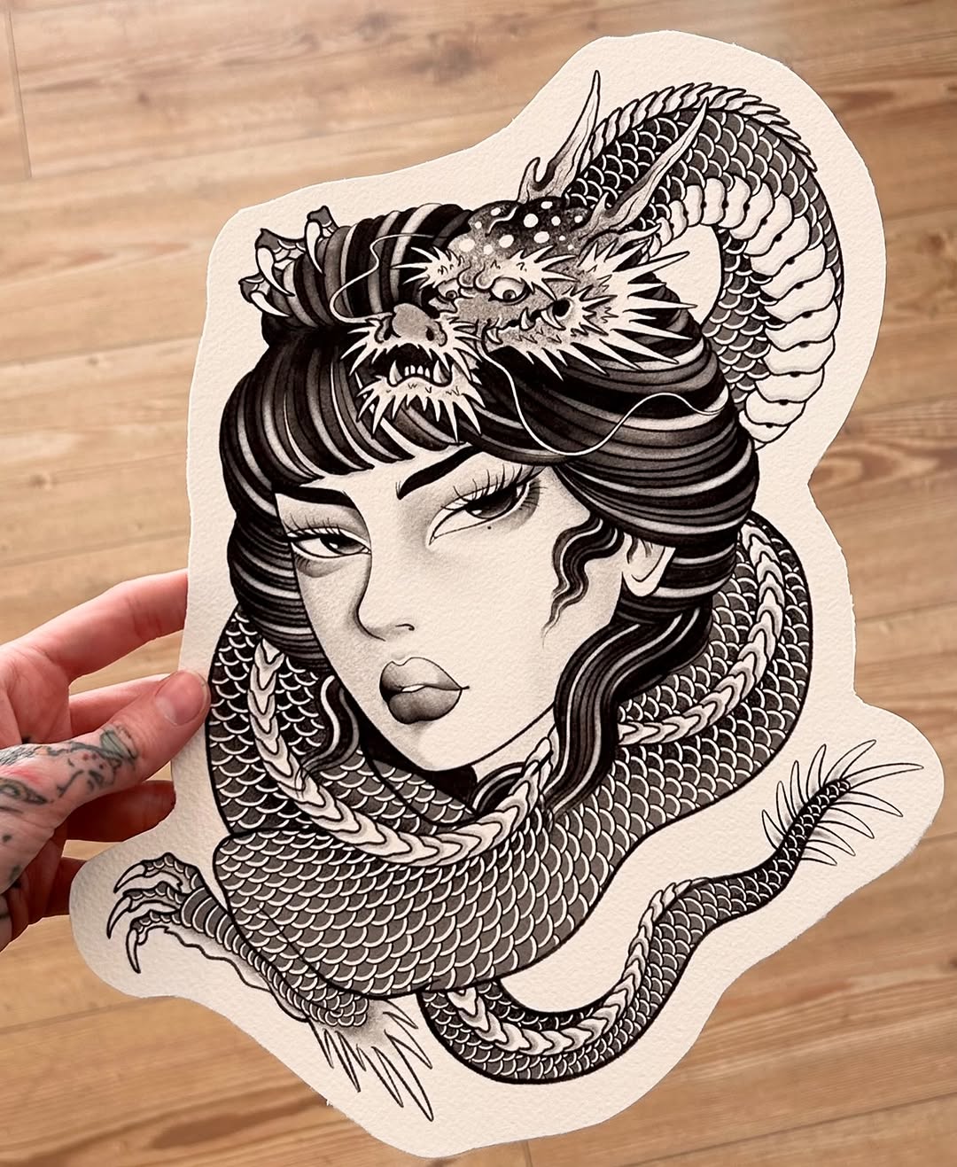 Intricate line drawing of a woman's face intertwined with a dragon, featuring detailed scales and shading in black ink on white paper.
