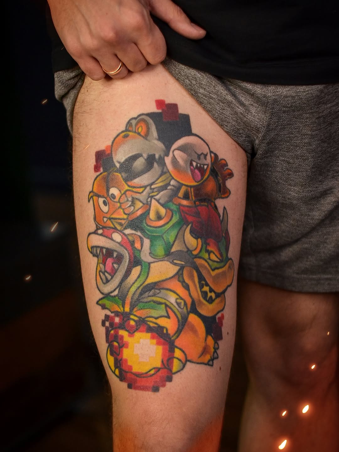 Colorful video game characters tattoo on thigh featuring stacked creatures in orange, green, yellow, and red with pixel-style elements.